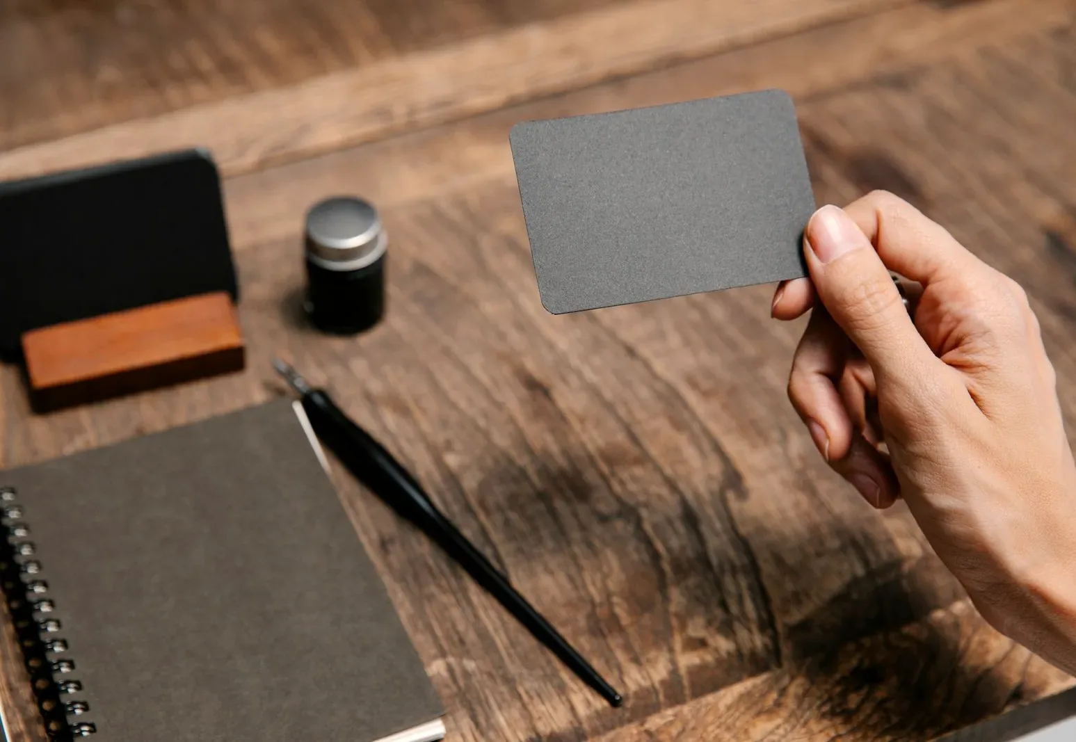 A hand holding a blank business card above a wooden café desk
