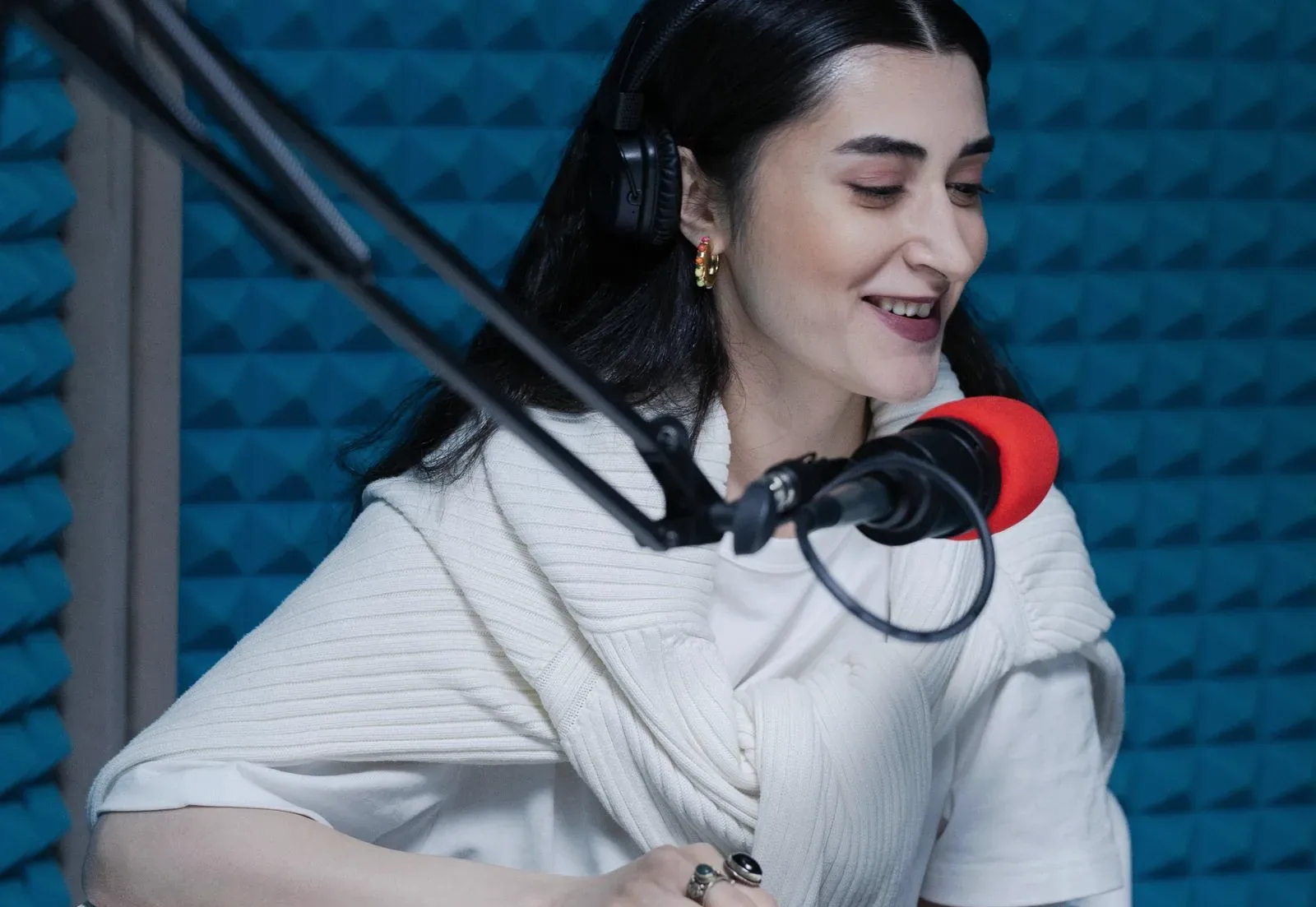 A podcaster smiling at a microphone in a treated studio